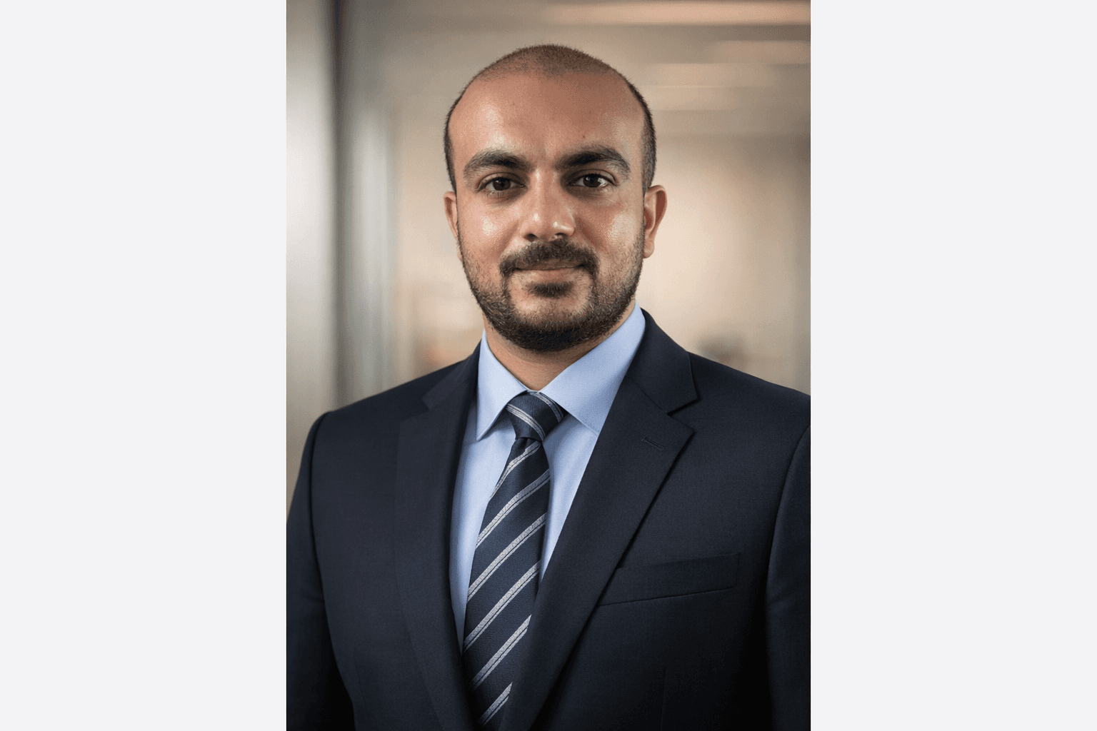 Professional headshot of a bearded man wearing a dark suit, blue shirt, and striped tie.
