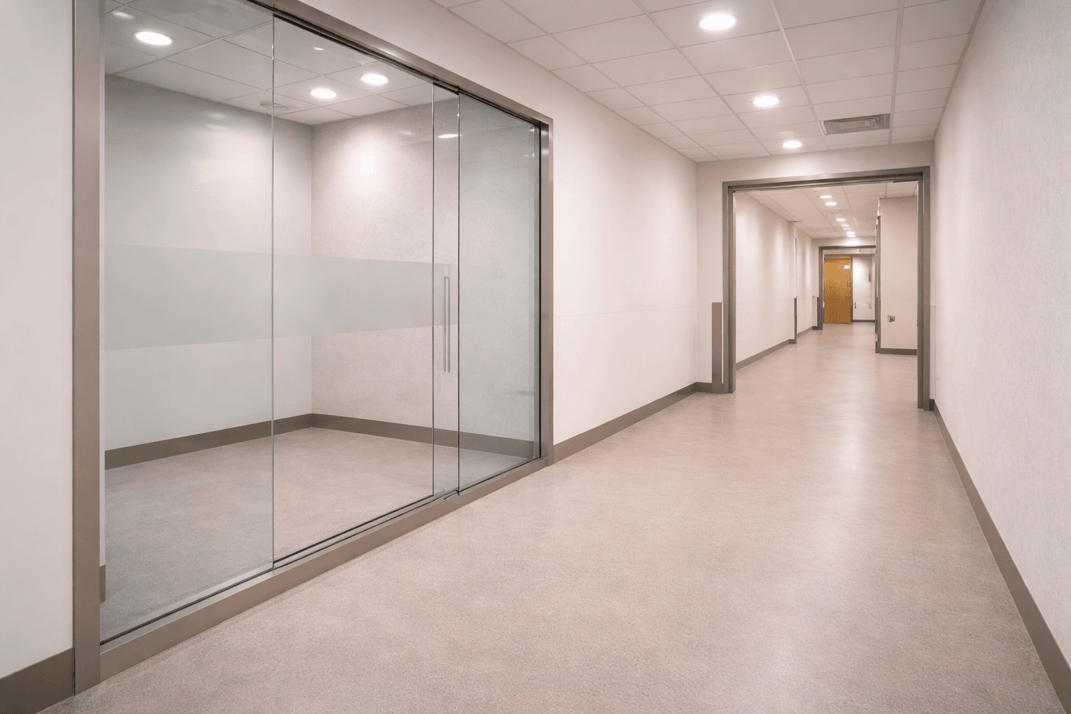 Brightly lit modern hallway featuring a glass-walled room with a frosted privacy strip.
